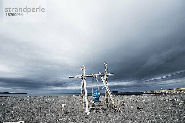 Ein Junge auf einer natürlichen Schaukel an der Nordküste Islands