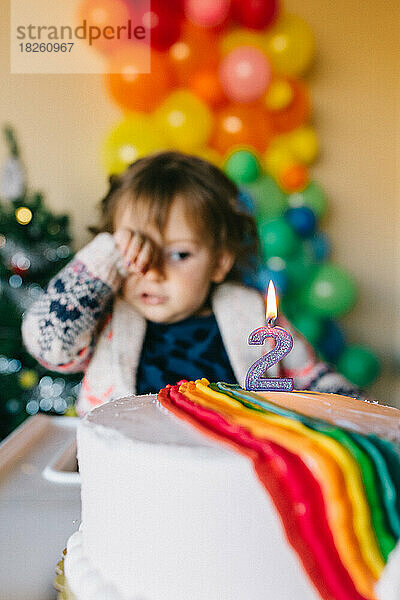 Kleines Mädchen schaut auf eine Regenbogen-Geburtstagstorte