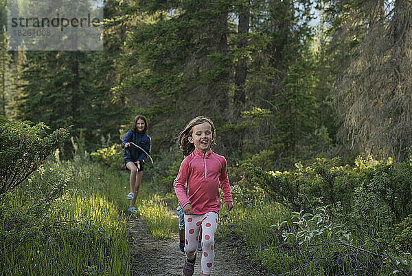 Ein junges Mädchen rennt mit anderen Kindern einen Pfad im Wald entlang