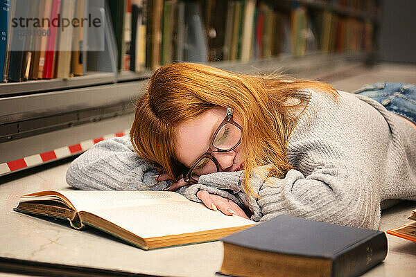 Teenie-Mädchen mit roten Haaren und Brille schläft beim Lernen.
