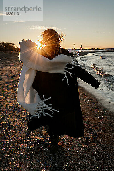 Ein junges Mädchen läuft am Strand entlang und der Schal an ihrem Mantel entwickelt sich.