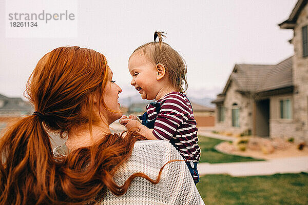 Baby lacht mit ihrer rothaarigen Mutter draußen beim Spaziergang