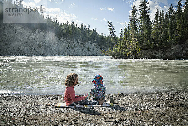 Zwei Kinder sitzen an einem Flussstrand