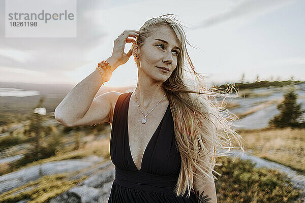 schöne junge Frau im Kleid mit windgepeitschten langen blonden Haaren bei Sonnenuntergang
