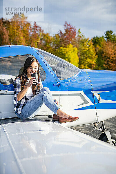 Junge BIPOC-Pilotin nippt am Morgenkaffee auf dem Flügel eines Kleinflugzeugs