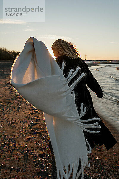 Ein junges Mädchen läuft am Strand entlang und der Schal an ihrem Mantel entwickelt sich.