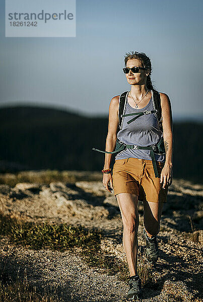 Frau in Shorts mit Sonnenbrille wandert bei Sonnenuntergang in Maine