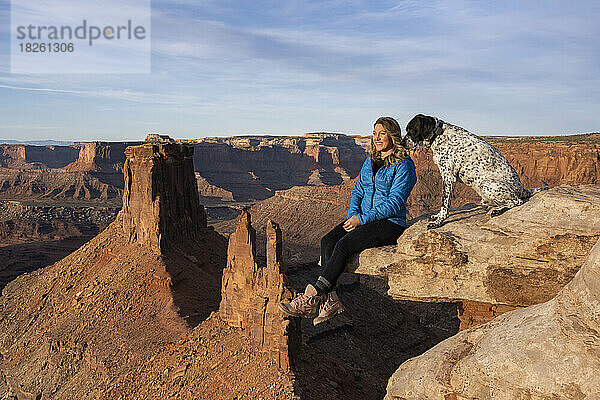 Glückliche Frau blickt auf die Aussicht  während sie neben einem Hund am Rande der Wüste sitzt