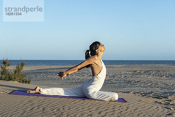 Seitenansicht einer Frau  die auf einer Matte am Strand Yoga praktiziert