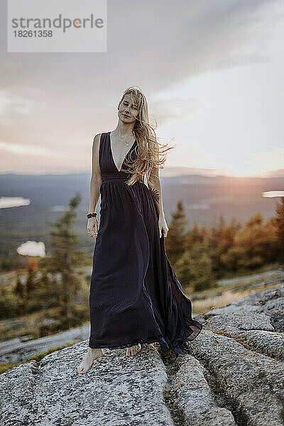 schöne blonde Frau barfuß in langem Kleid mit Tätowierung bei Sonnenuntergang