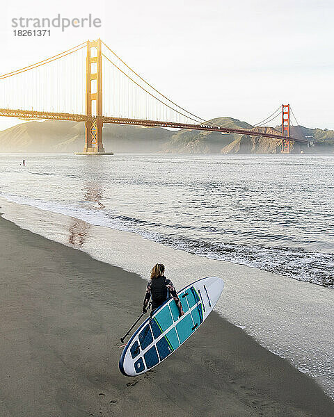 Frau mit Paddleboard läuft in Richtung Golden Gate Bridge