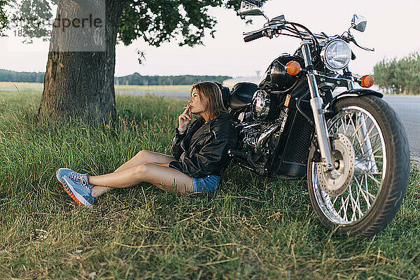 Junge Frau mit einer Zigarette sitzt neben einem Motorrad