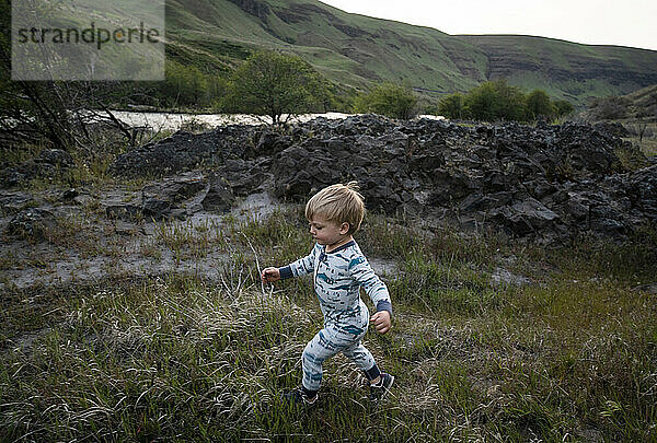 Ein kleiner Junge im Pyjama rennt in der Abenddämmerung durch Gras in der Nähe eines Flusses