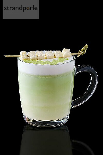 Matcha Latte mit Kokosnussstückchen am Spieß auf schwarzem Hintergrund