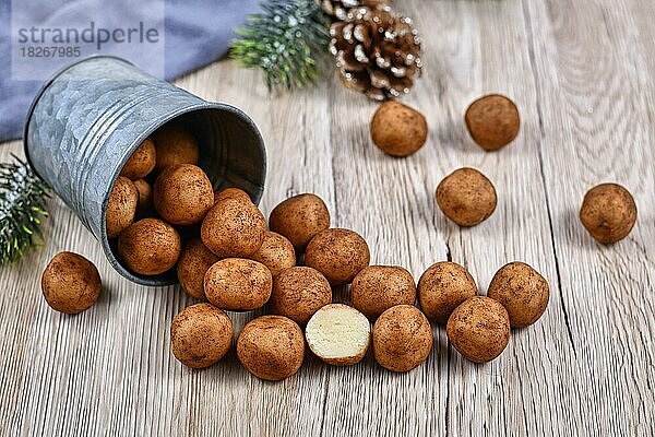 Traditionelle deutsche Weihnachtssüßigkeiten  genannt Marzipankartoffeln. Runde  kugelförmige  mit Zimt und Kakaopulver bestreute Mandelpastetchen  die aus einem Eisenbecher auf Holzuntergrund quellen