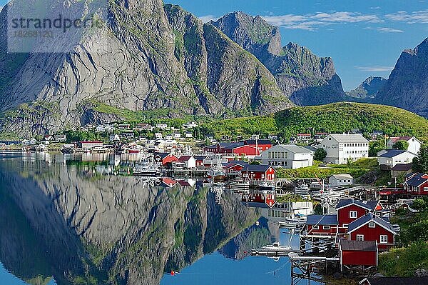 Ortsansicht  Reinefjord mit Bergen und roten Holzhäusern  Häuser und Berge spiegeln sich im Fjord  Reine  Moskenesöy  Lofoten  Nordland  Norwegen  Europa