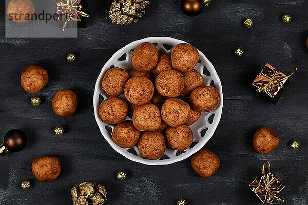 Traditionelle deutsche Weihnachtsbonbons  genannt Marzipankartoffeln. Runde  kugelförmige Marzipankartoffeln mit Zimt und Kakaopulver in einer weißen Schale auf dunklem Hintergrund