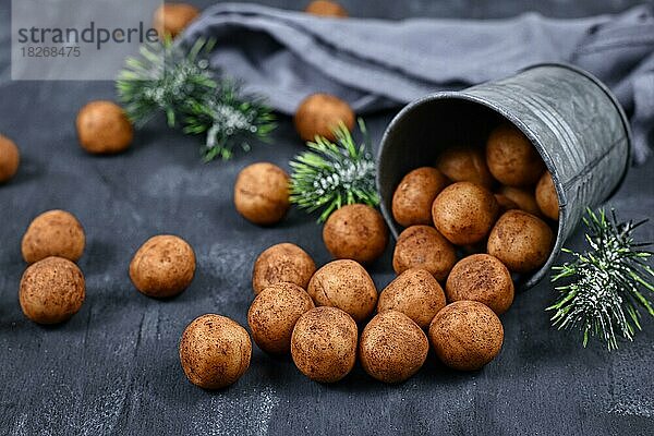 Traditionelle deutsche Weihnachtssüßigkeiten  genannt Marzipankartoffeln. Runde  kugelförmige  mit Zimt und Kakaopulver überzogene Mandelpastetenstücke  die aus einer Eisenschale auf dunklem Hintergrund herausquellen