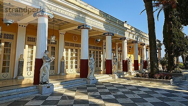 Achilleion  Wohnort Kaiserin Sissis  1889 fertig gebaut  Architektur an die griechische Mythologie angelehnt  Terrasse  Weitwinkelaufnahme  rot-weiße Säulen  davor einige Marmorstatuen der Musen  schachbrettartiger Mosaikboden  blauer Himmel  Insel Korfu  Ionische Inseln  Griechenland  Europa