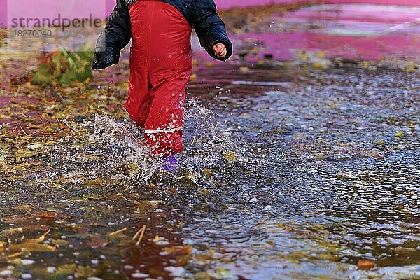 Kind spritzt mit Stiefeln und Wasserhose in einer Pfütze an einem regnerischen Tag mit Wasser