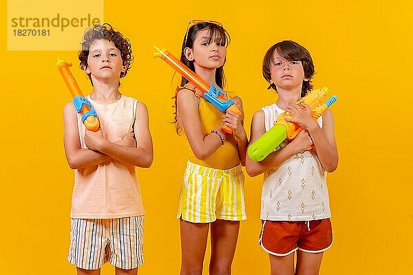 Kinder mit Wasserpistolen im Sommerurlaub  gelber Hintergrund
