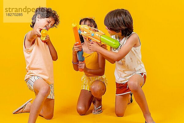 Kinder haben Spaß mit Wasserpistolen in den Sommerferien und zielen auf die Kamera  gelber Hintergrund
