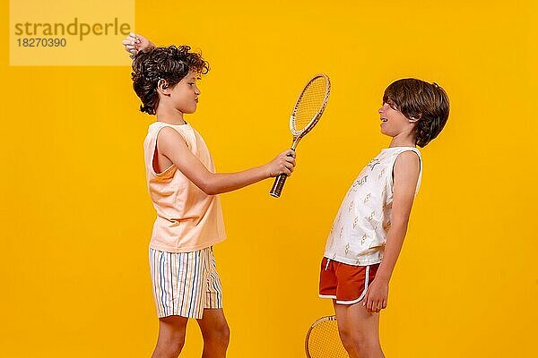 Zwei Kinder spielen Tennis und haben Spaß  gelber Hintergrund