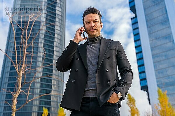 Corporate Porträt der kaukasischen Geschäftsmann am Telefon neben Wolkenkratzer Büro sprechen