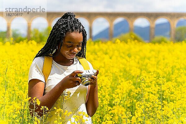 Ich schaue mir die Fotos auf einer alten Kamera an  ein schwarzes ethnisches Mädchen mit Zöpfen  eine Reisende  in einem Feld mit gelben Blumen