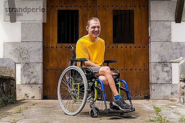 Porträt eines gelb gekleideten Behinderten in einem Rollstuhl im Eingang seines Hauses  der lächelt