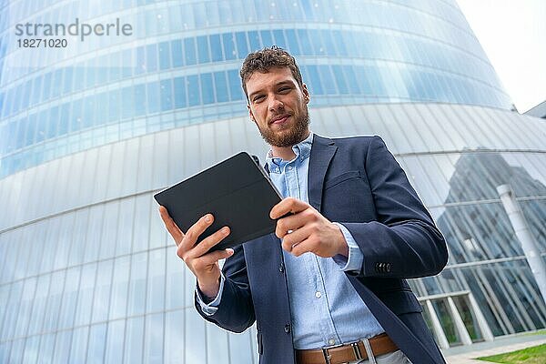 Porträt eines männlichen Geschäftsmannes oder Unternehmers außerhalb des Büros  der ein Tablet in einem Glasgebäude benutzt