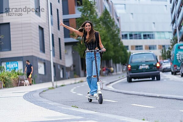 Eine junge brünette Frau  die sich mit einem Elektroroller in der Stadt bewegt und Spaß hat  entlang des Radwegs