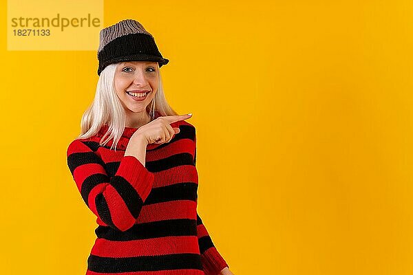 Zeigen Sie rechts Winter themed blonde kaukasische Mädchen auf gelben Studio Hintergrund