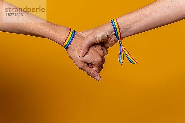 Detail von zwei Händen von zwei Frauen schütteln Hände mit einem Armband  LGBT-Konzept auf einem gelben Hintergrund  Paar lesbische Mädchen