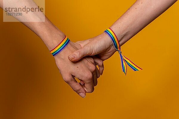 Detail von zwei Händen von zwei Frauen schütteln Hände mit einem Armband  LGBT-Konzept auf einem gelben Hintergrund  Paar lesbische Mädchen