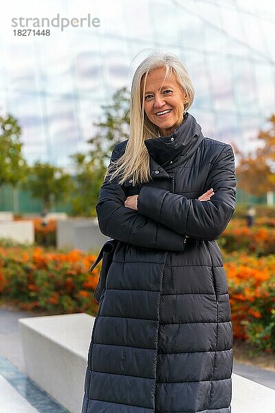 Unternehmensporträt einer weißhaarigen Geschäftsfrau mittleren Alters  stehend vor einem Wolkenkratzer-Büro