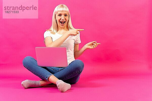 Blondes kaukasisches Mädchen mit einem Computer  Studioaufnahme auf rosa Hintergrund  Kopierraum  zeigend