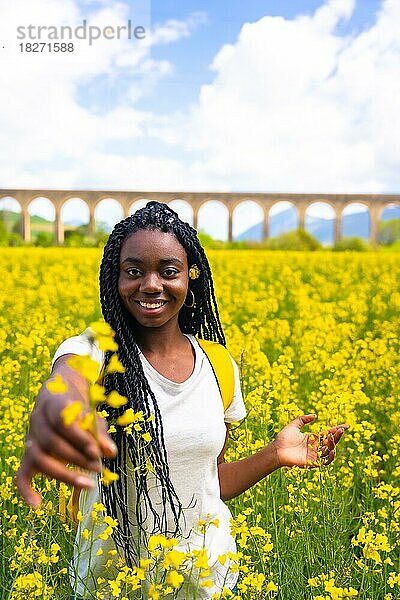 Lächelnd in der Natur  ein Mädchen schwarzer Ethnie mit Zöpfen  eine Reisende  in einem Feld mit gelben Blumen