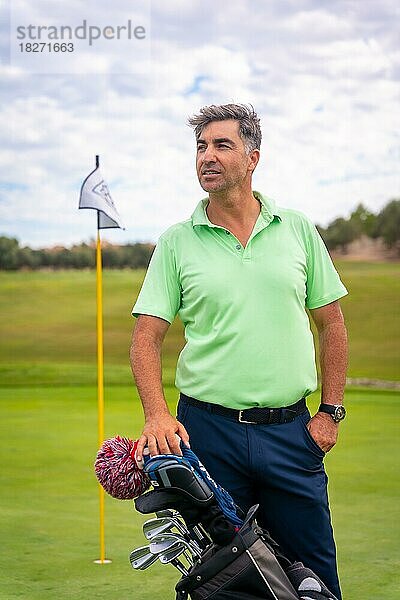 Porträt eines Mannes  der zusammen mit seinen Schlägern auf dem Grün Golf spielt und den Sport genießt