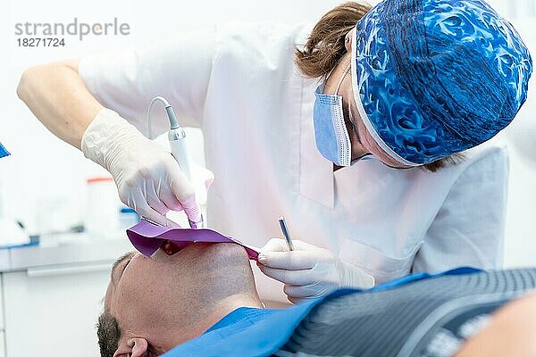 Zahnklinik  ein Arzt führt eine Wurzelbehandlung an einem Patienten in voller Aktion durch