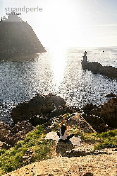 Eine Frau macht Yogaübungen in der Natur am Meer  Virasana oder Ardha Padmasana