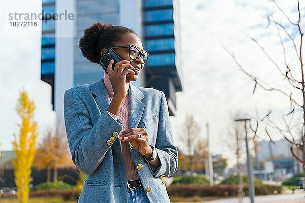 Porträt einer schwarzen ethnischen Geschäftsfrau mit Brille in einem Gewerbegebiet  die lächelnd telefoniert