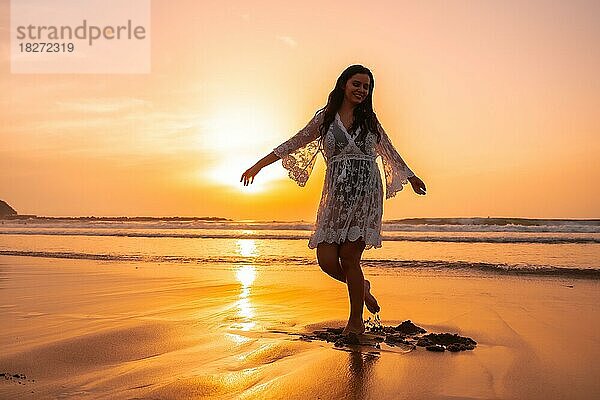 Silhouette einer Frau am Strand bei Sonnenuntergang in einem weißen Kleid