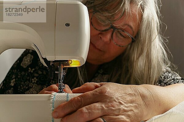 Ältere Frau mit weißem Haar  unscharf  näht einen weißen Stoff auf einer Nähmaschine
