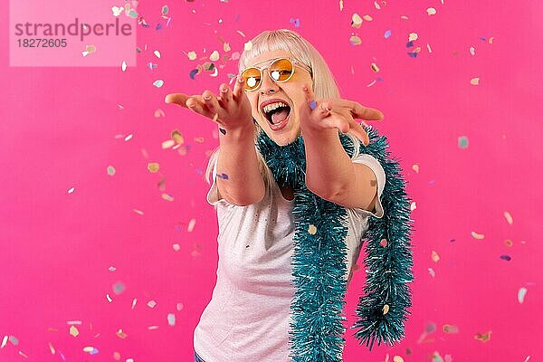 Lächelnd auf einer Party werfen Konfetti in Sonnenbrille  blonde kaukasische Mädchen auf rosa Hintergrund Studio