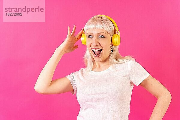 Blondes kaukasisches Mädchen im Studio auf rosa Hintergrund  lächelnd  hört Musik mit Kopfhörern