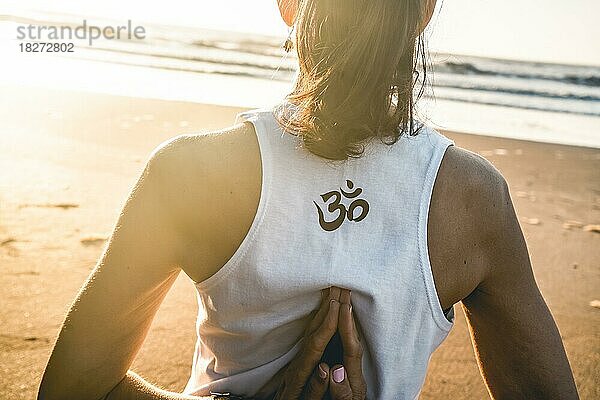 Rückansicht einer jungen Frau  die am Strand Yoga übt