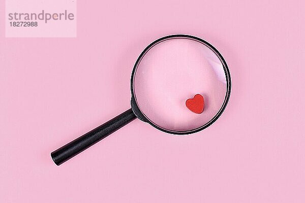 Konzept für die Suche nach Liebe mit Lupe und rotem Herz-Symbol auf rosa Hintergrund