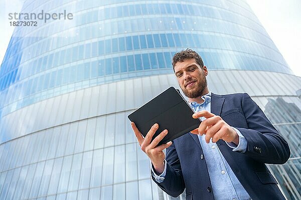 Männlicher Geschäftsmann oder Unternehmer außerhalb des Büros  der ein Tablet in einem Glasgebäude benutzt