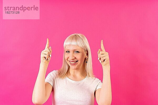 Blondes kaukasisches Mädchen Studioaufnahme auf rosa Hintergrund  Kopierraum  lächelnd nach oben zeigend